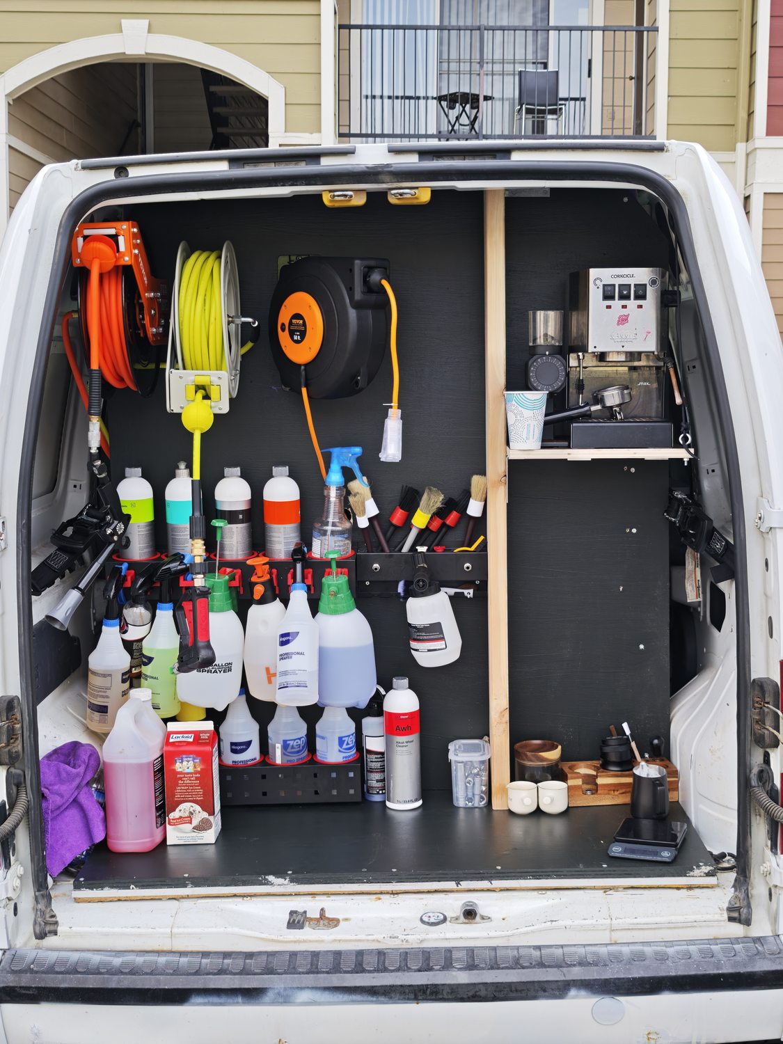 The whole back of the detailing van — hose reels, chemicals, brushes and the espresso corner, all on board